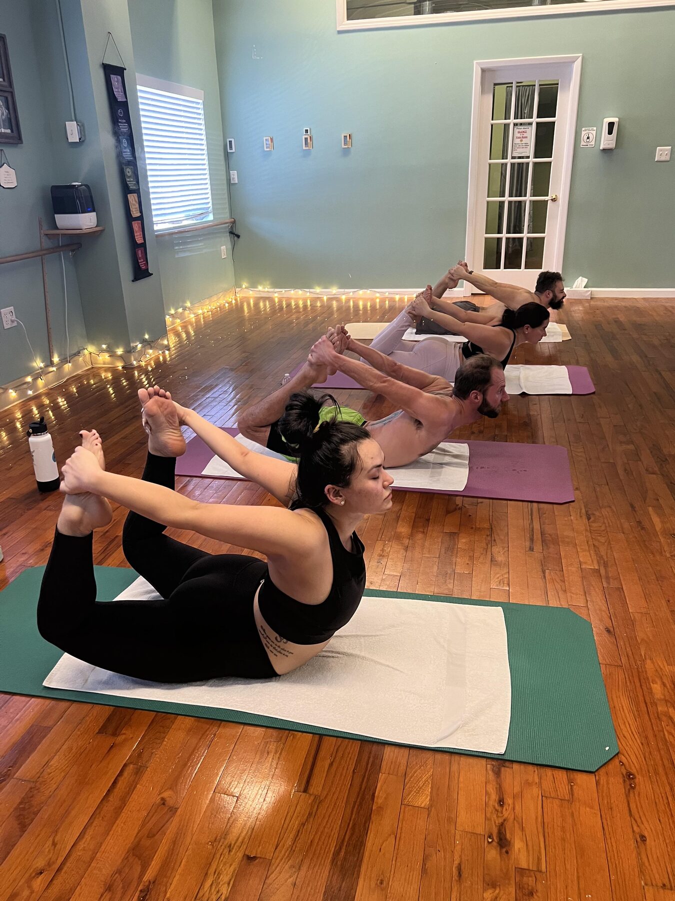 Group yoga class in bow pose by string lights